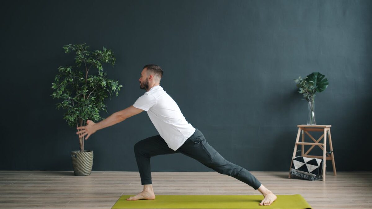 A man practicing yoga indoors on a green mat, focusing on balance and flexibility.