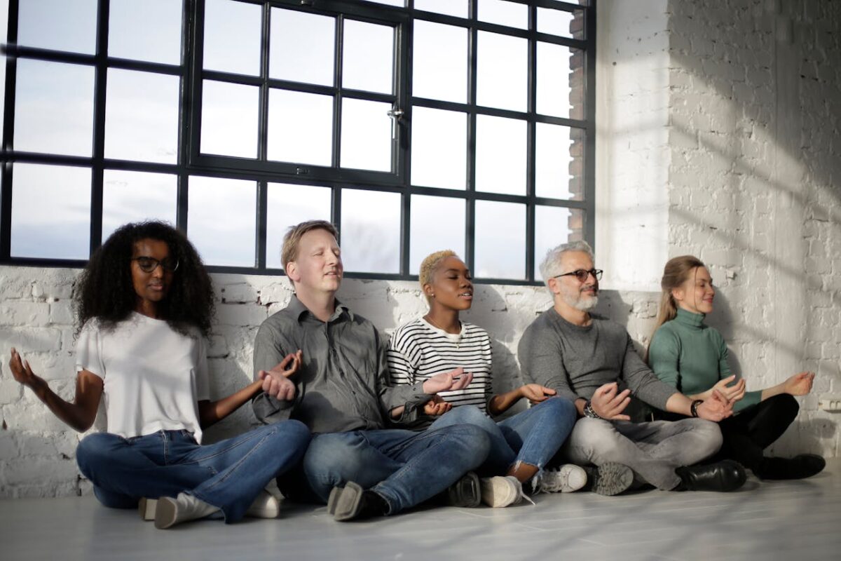 Calm smiling multiethnic friends sitting in lotus pose on floor while relaxing with closed eyes in loft styled room